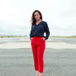 Full-body portrait of a fashionable woman in red trousers and polka dot blouse outdoors.