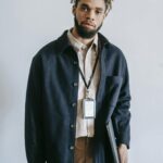 Portrait of a confident young African American man with laptop and bag, standing indoors.